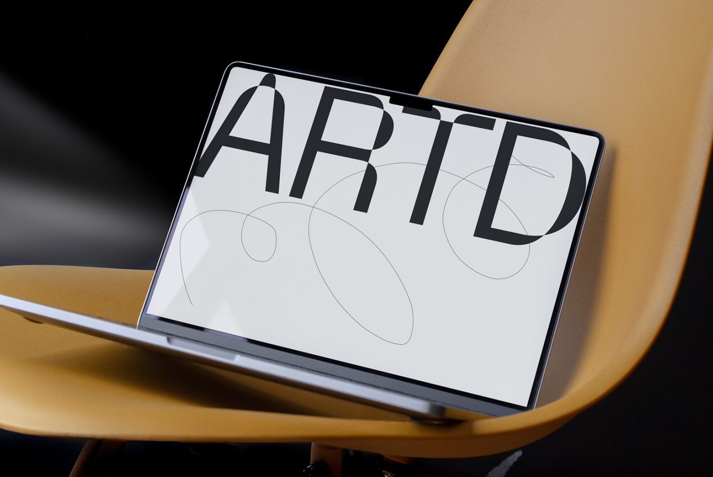 Laptop on a yellow chair displaying bold ARTD font design, with abstract graphics, ideal for template and font mockup presentations.